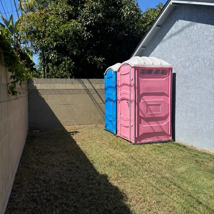 Blue and pink porta potties set on a backyard lawn beside a house