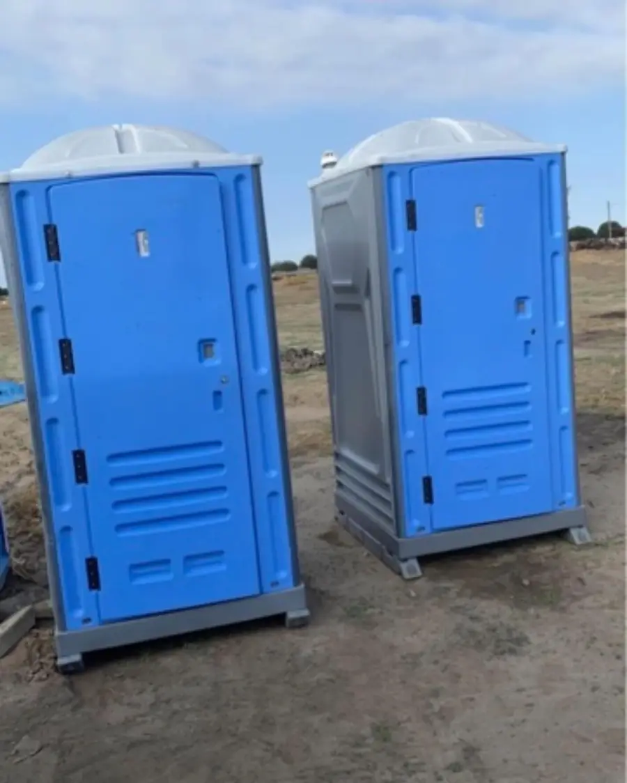 Two porta potties on a dirt construction lot under a clear sky