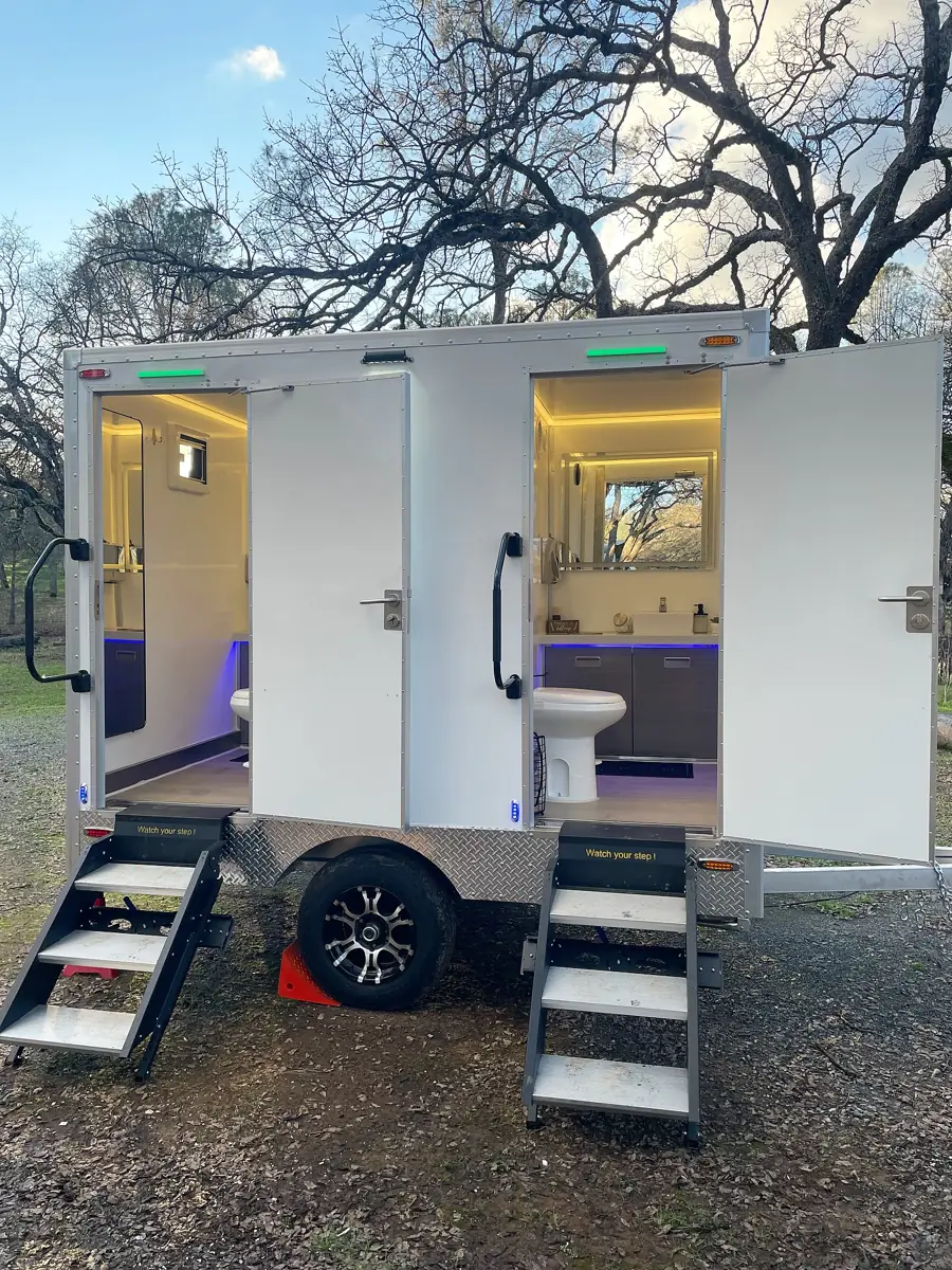 Lit two-room restroom trailer set up outdoors at an evening event